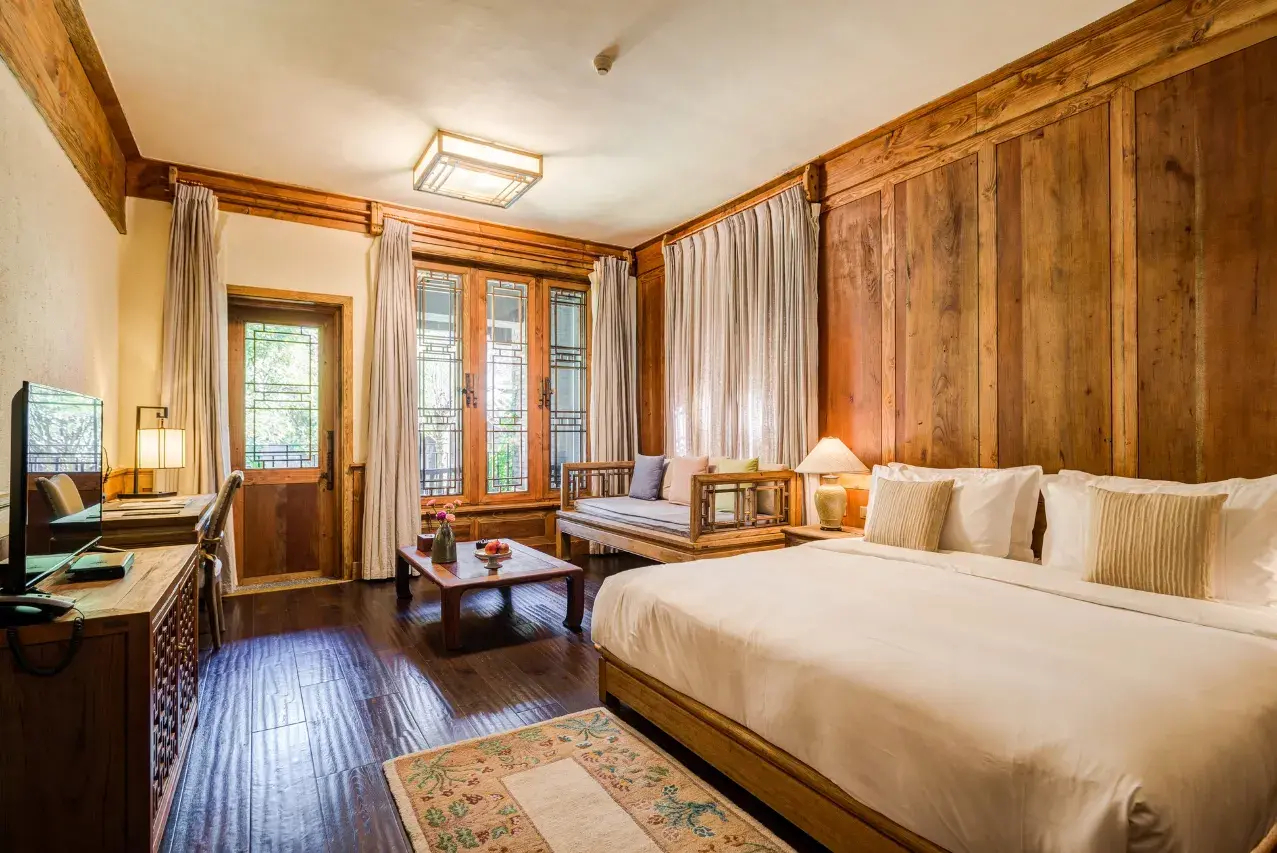 Guest room with timber-panelled walls, king bed, daybed and latticed windows over dark wood floors.