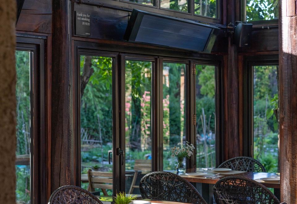 The Bivou — the glass-walled garden lounge in restored dark timber, rattan chairs at a set table looking onto the planted courtyard, Shuhe