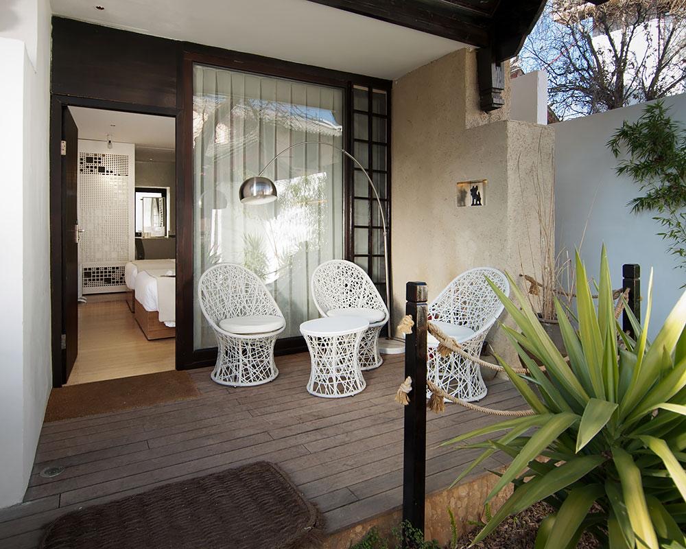 The Bivou — a guest room's private deck terrace with woven chairs opening onto the bedroom and garden planting, Shuhe, Lijiang