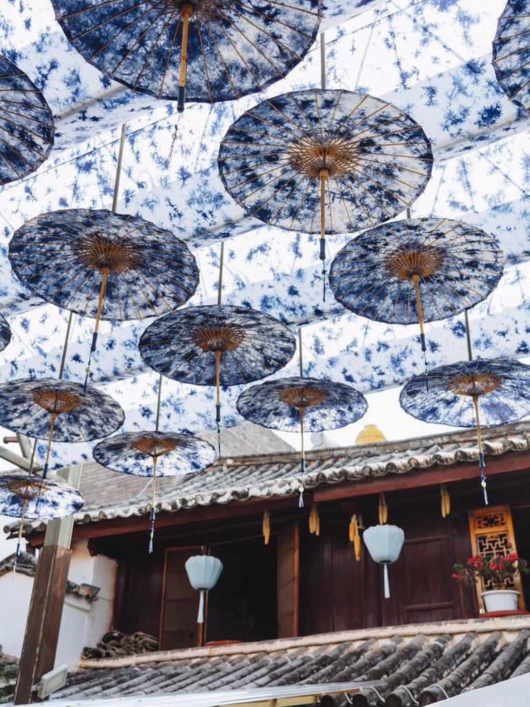 Canopy of blue-and-white tie-dye paper parasols suspended above a tiled traditional courtyard roof.