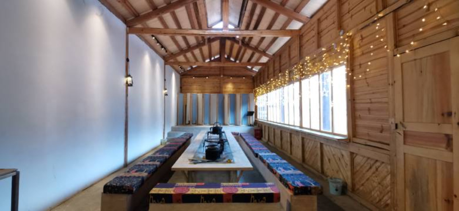 Tianyu Tacheng — long communal dining table on patterned benches beneath an exposed pine roof
