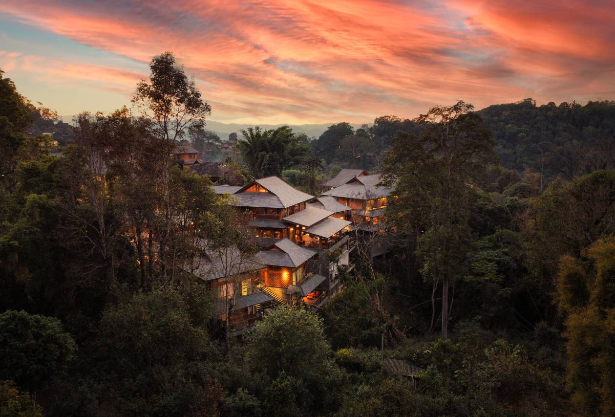 Vipaxana (方物之外·阿百腊) — timber pavilions with pitched Bulang roofs on the forested ridge at sunset, Jingmai Mountain