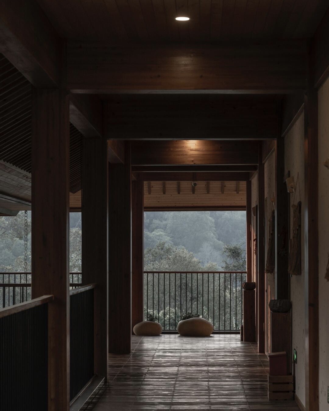 Dim timber corridor opening onto a balcony with floor cushions and a misty forested valley beyond.