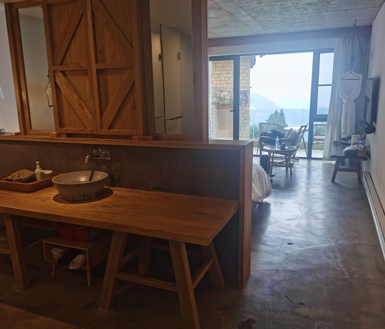 Yuanshe Azheke — a guest room's timber vanity with a stone basin, glass doors opening to a balcony over the misty valley