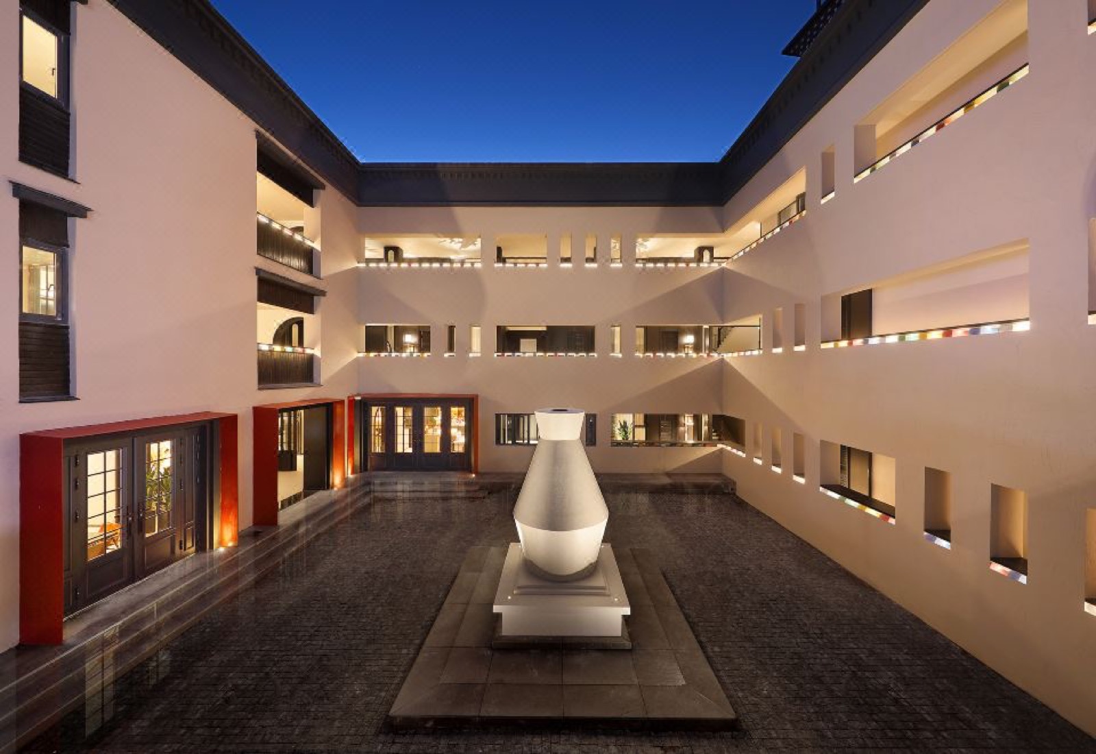Z Hotel Supreme · Feilai Si — the pale-plastered courtyard at blue-hour dusk, a white vase sculpture at its centre and coloured glass-brick openings ringing the upper floors