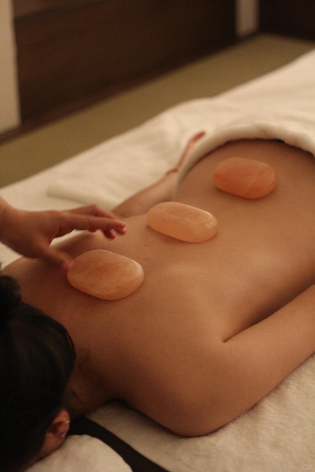 Spa therapist placing warm translucent stones along a guest's back during a hot-stone massage.