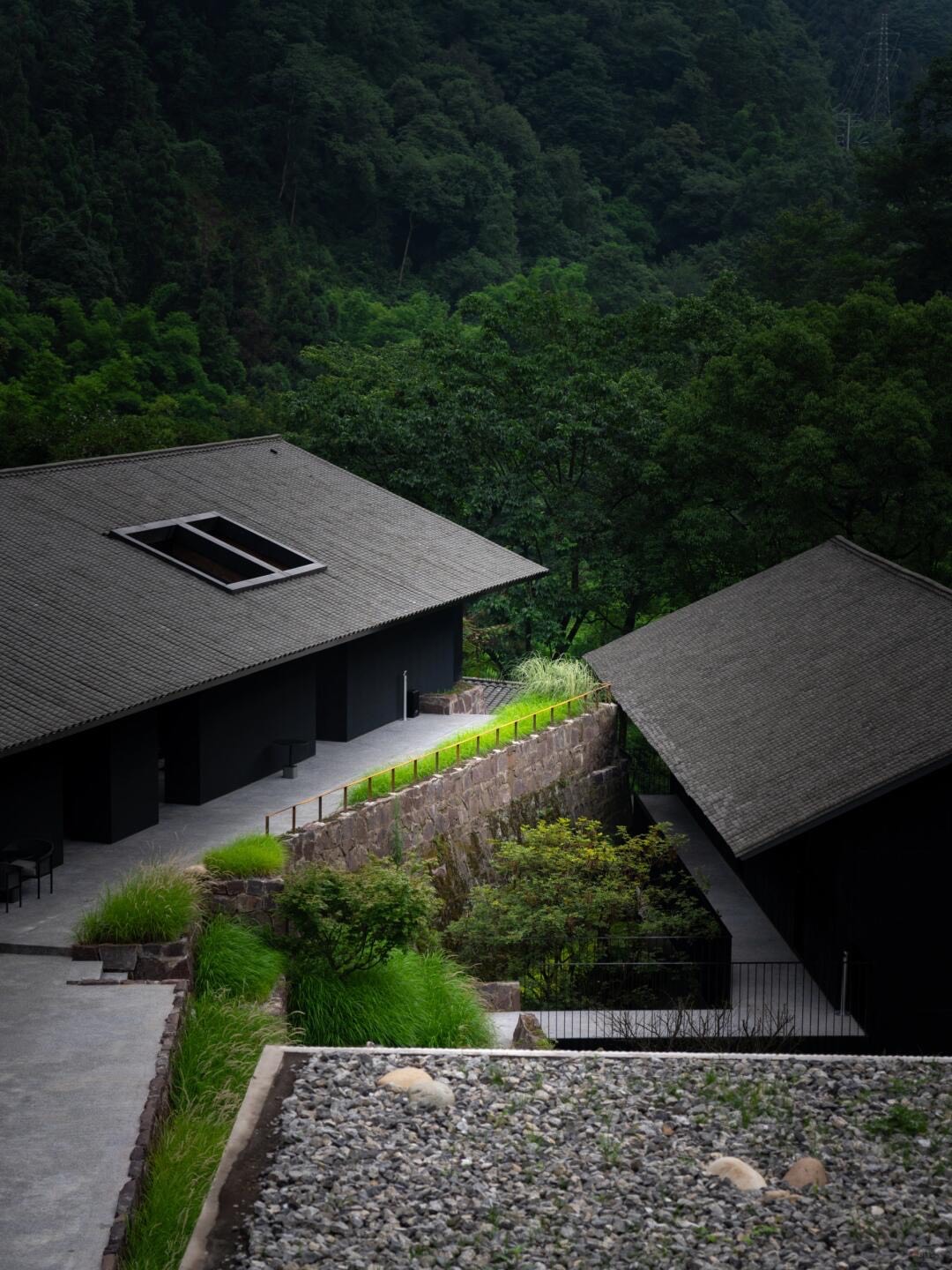 Grey tiled-roof villas stepping down a forested hillside with stone retaining walls and planted terraces between them.