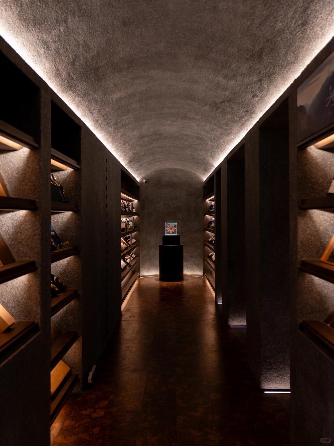Dark vaulted corridor with backlit stone shelving leading to a single illuminated display plinth.
