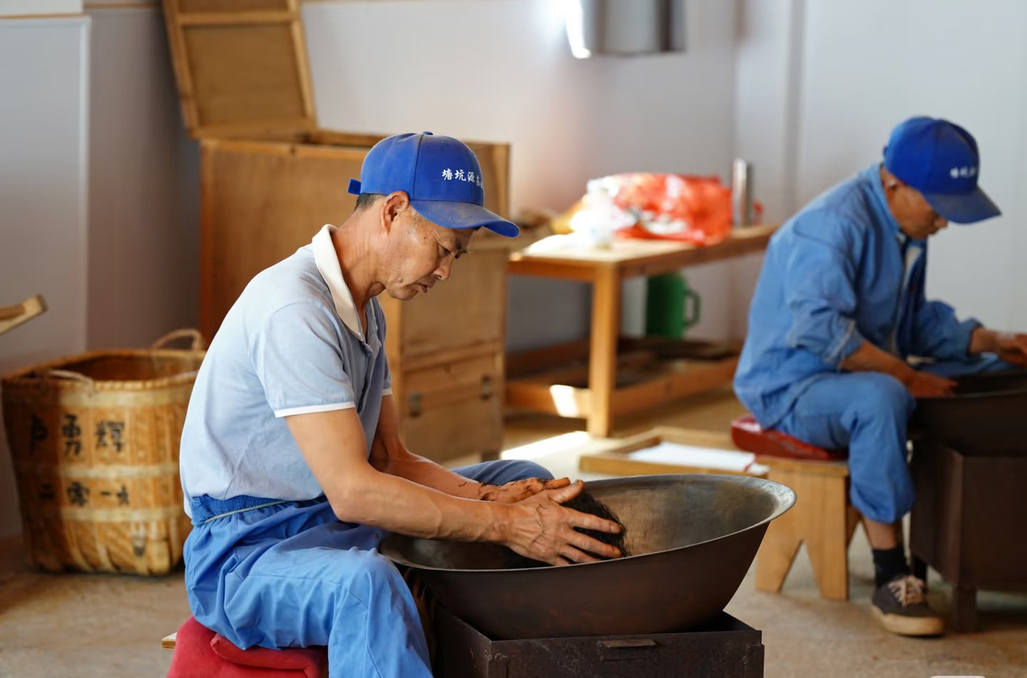 Two tea makers hand-firing leaves in iron woks