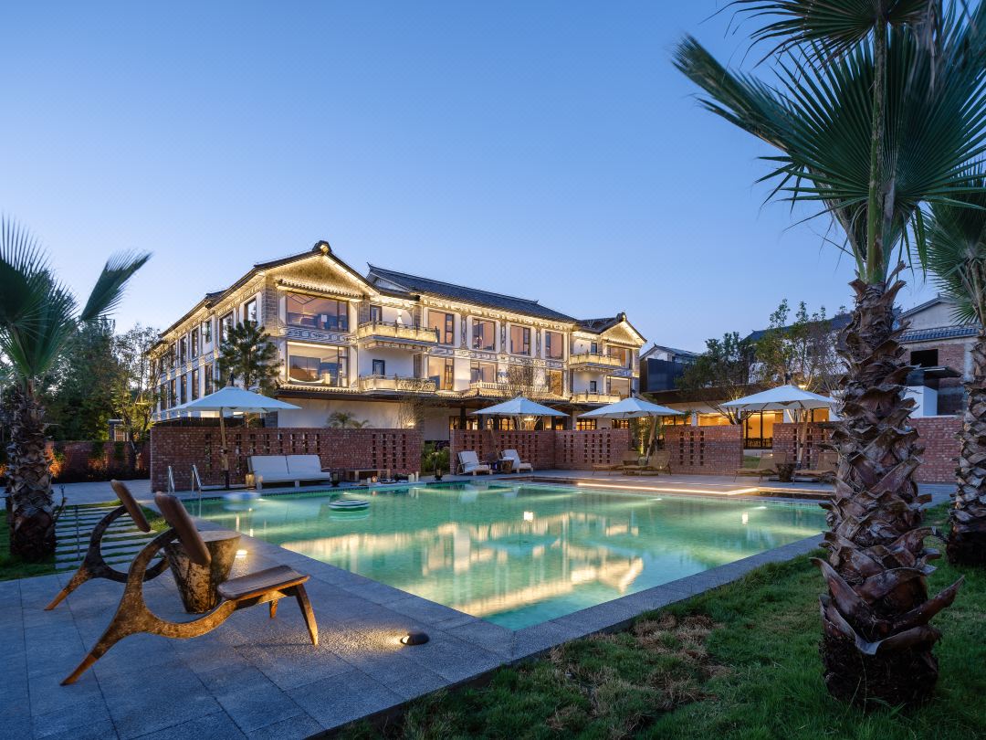 Kaichen Hotel — the heated pool and Bai-style main house at dusk